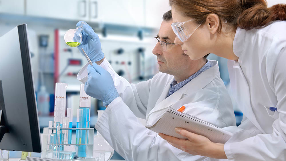 Perfil de um cientista segurando um recipiente de química e uma cientista observando ao seu lado.