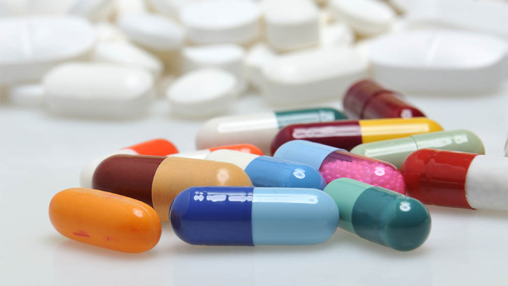 Cápsulas de medicamentos de diversas cores espalhadas em superfície.