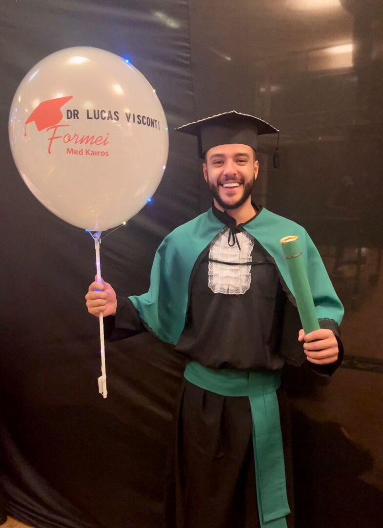 Foto mostra Lucas Visconti em sua formatura segurando um balão e o canudo de formatura.