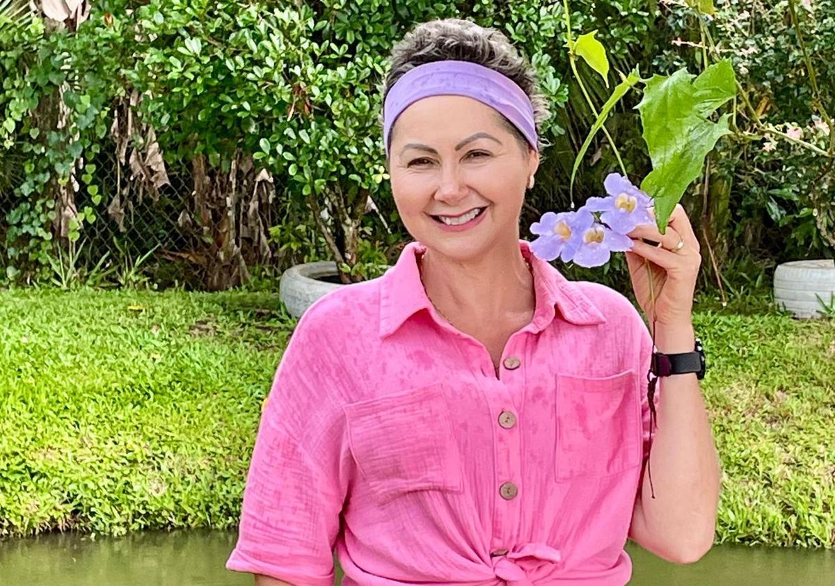 Adelma Cani Regis, participante de pesquisa clínica, sorrindo e segurando flores lilás em um jardim